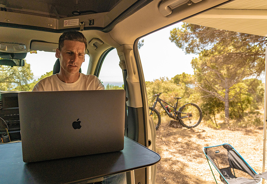 Crosscamper innen: Mann sitzt an Tisch und arbeitet mit Laptop