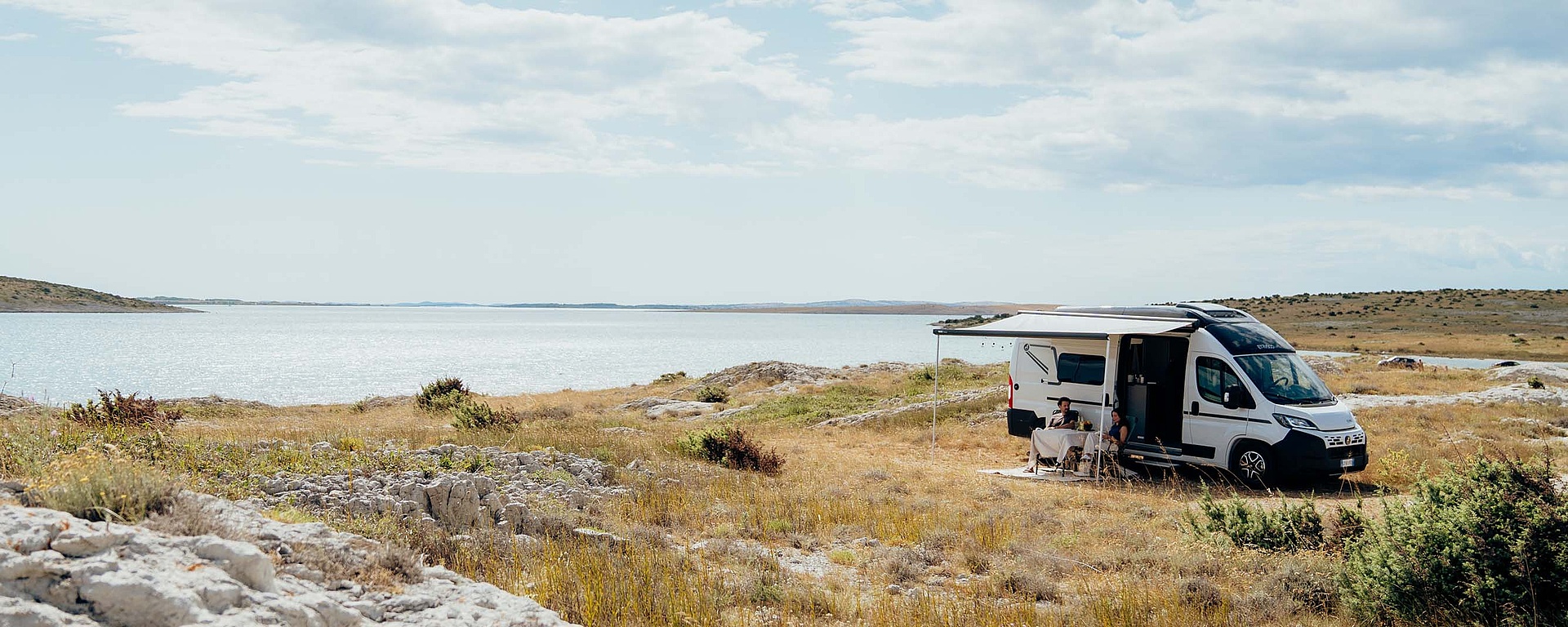 Pärchen sitzt vor einem Campervan mit Blick auf einen See