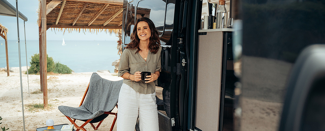 Frau vor Wohnmobil auf Campingplatz am Meer