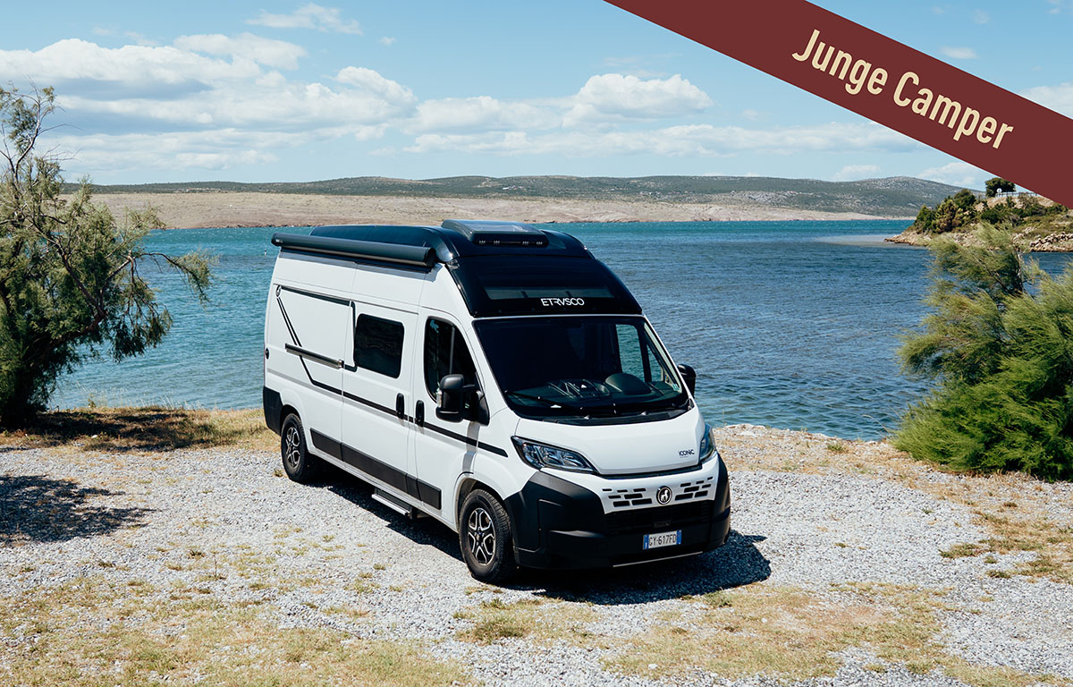 Ein weißer Etrusco Camper steht auf einem Schotterplatz neben einem See
